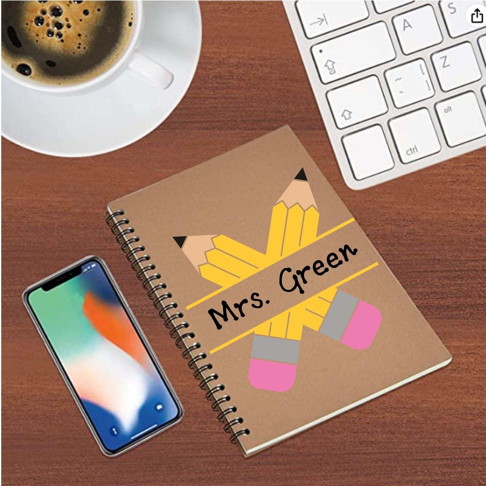 Personalised pencil teacher notebook with spiral binding on a desk near a smartphone and coffee.