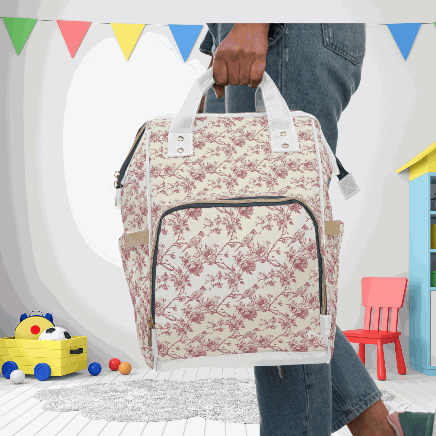 Pink toile diaper multifunctional backpack with floral pattern, held by a person in a colorful playroom setting.