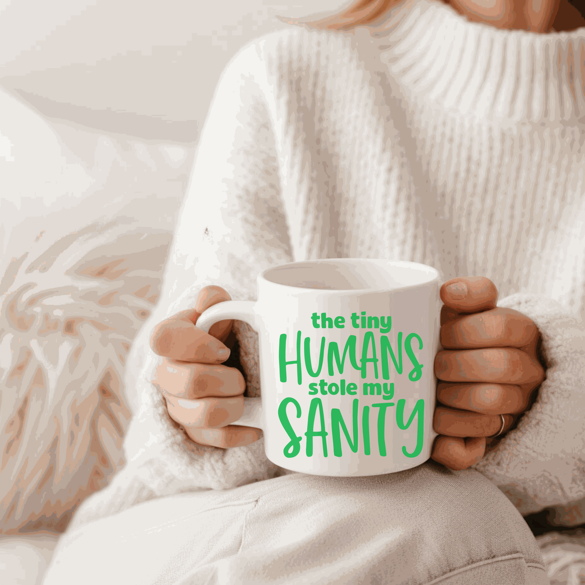 Funny ceramic mug with "The Tiny Humans Stole My Sanity" text, held by person in white sweater.