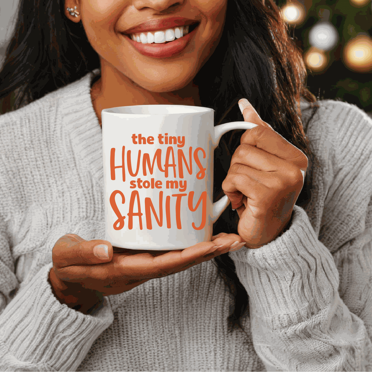 Ceramic mug with "The Tiny Humans Stole my Sanity" text, held by a smiling person wearing a gray sweater.