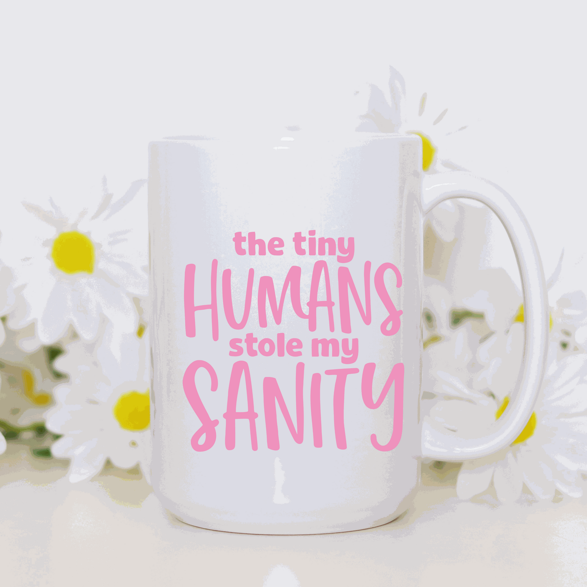 Ceramic mug with "The Tiny Humans Stole my Sanity" in pink letters, set against white with flowers in the background.