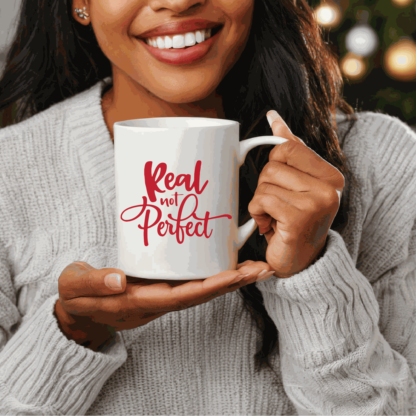 Ceramic coffee mug with "Real Not Perfect" in red lettering held by a smiling person.