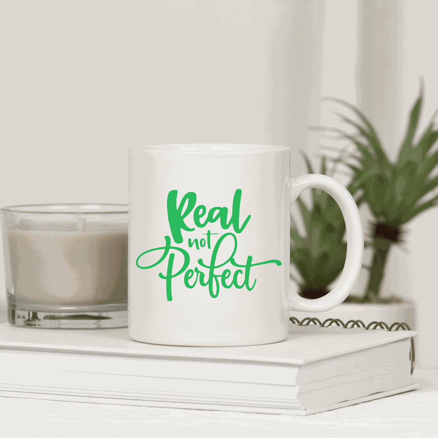 Ceramic coffee mug with "Real Not Perfect" quote in green text.