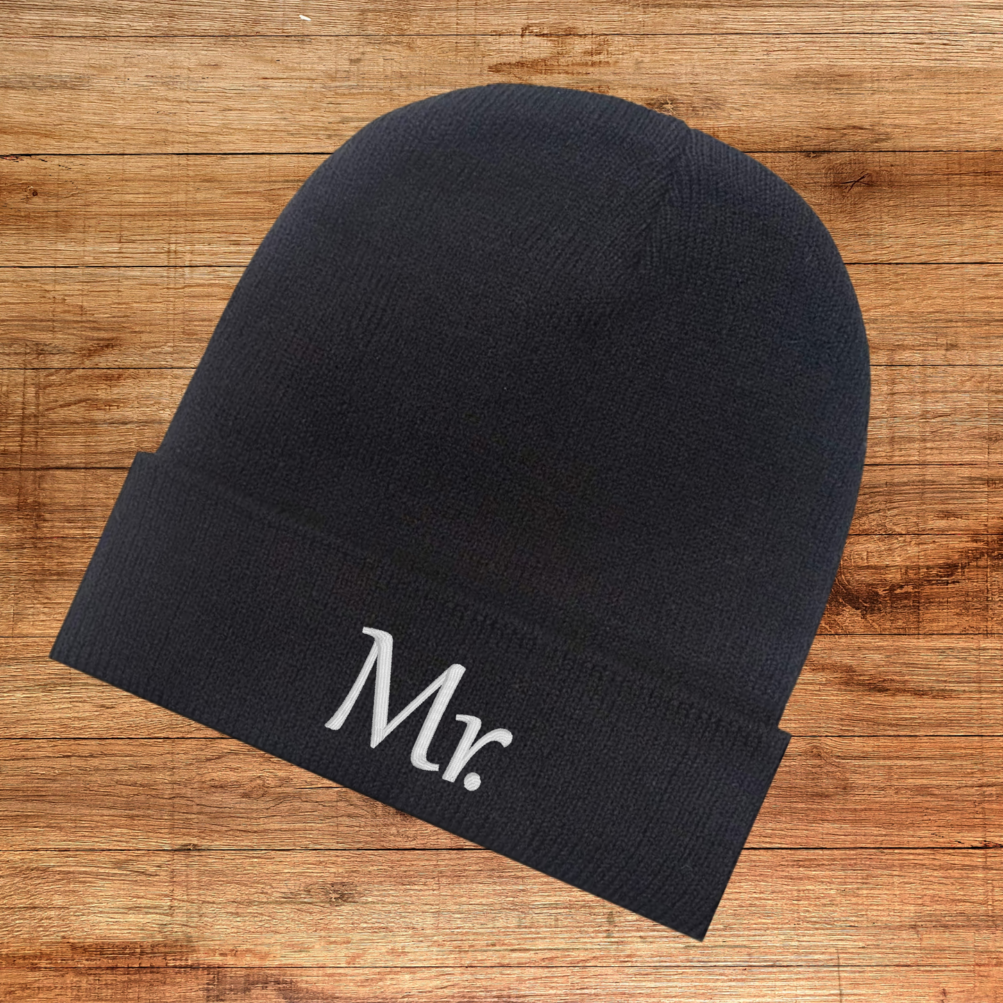 Mr. embroidered black beanie with folding cuff on wooden background.