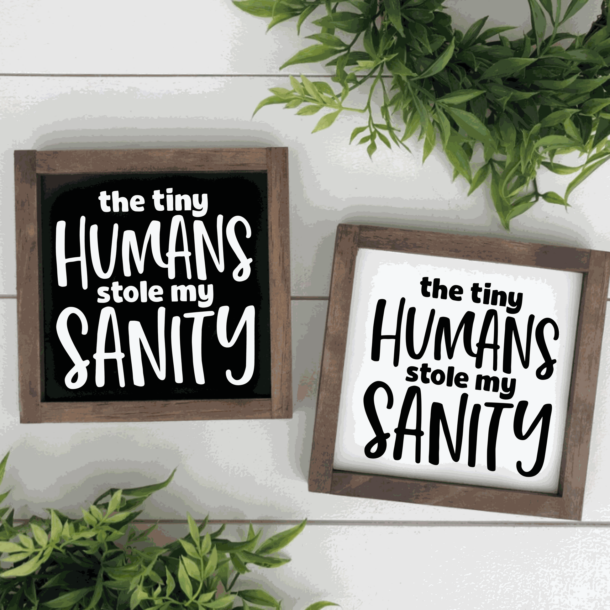 Wood signs with "The Tiny Humans Stole my Sanity" text in black and white options, surrounded by greenery.