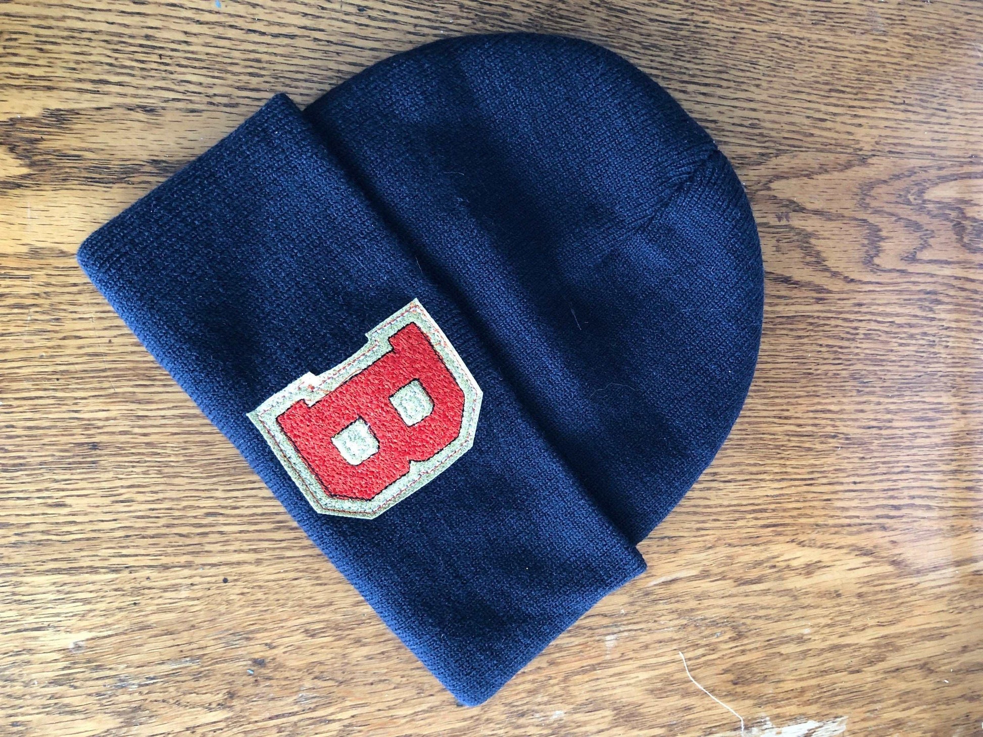 Custom embroidered initial beanie with fold-over design, displayed on a wooden surface.