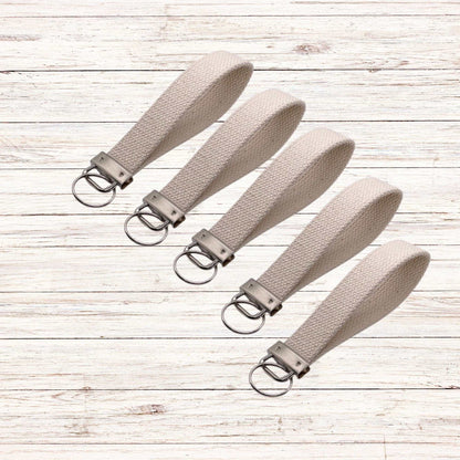 Natural beige cotton canvas keychains with metal hardware arranged on wooden surface
