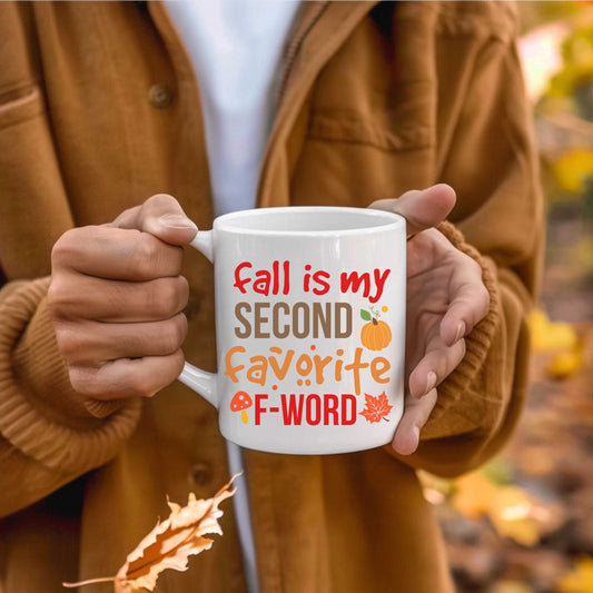 white ceramic mug with "Fall is my second favourite F word" text and autumn-themed graphics held by person in brown jacket