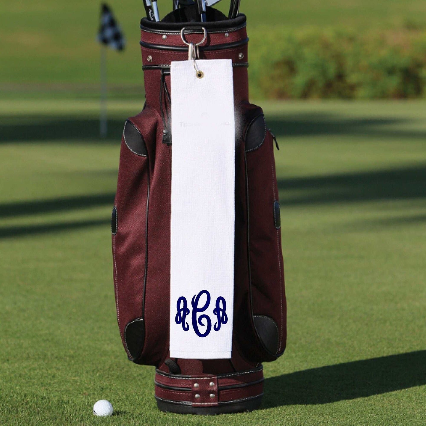 Personalized golf towel with custom embroidered monogram hanging on a golf bag, made from 100% cotton terry cloth.