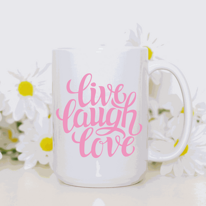 White ceramic coffee mug with "Live Love Laugh" in pink script font, surrounded by daisies.