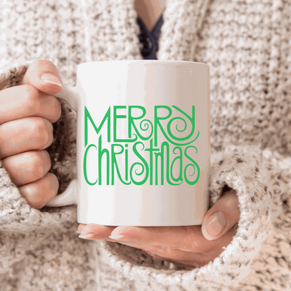 Merry Christmas ceramic mug with green festive text design, held by a person in a cozy sweater.