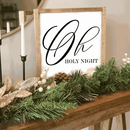 Oh Holy Night Christmas wood sign with white background and black lettering, framed with stained wood, decorated with greenery and candles.