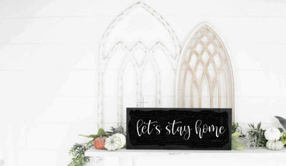 Let's Stay Home rustic wood sign with black background and white lettering, displayed on a decorative shelf.