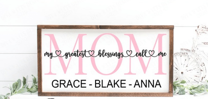 Personalized wood sign with "My Greatest Blessings Call Me Mom" design and children's names, featuring a white background and wooden frame.