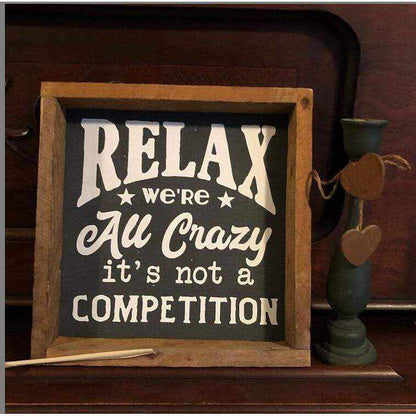 Framed wood sign with "Relax We're All Crazy It's Not A Competition" on black background with natural wood frame.